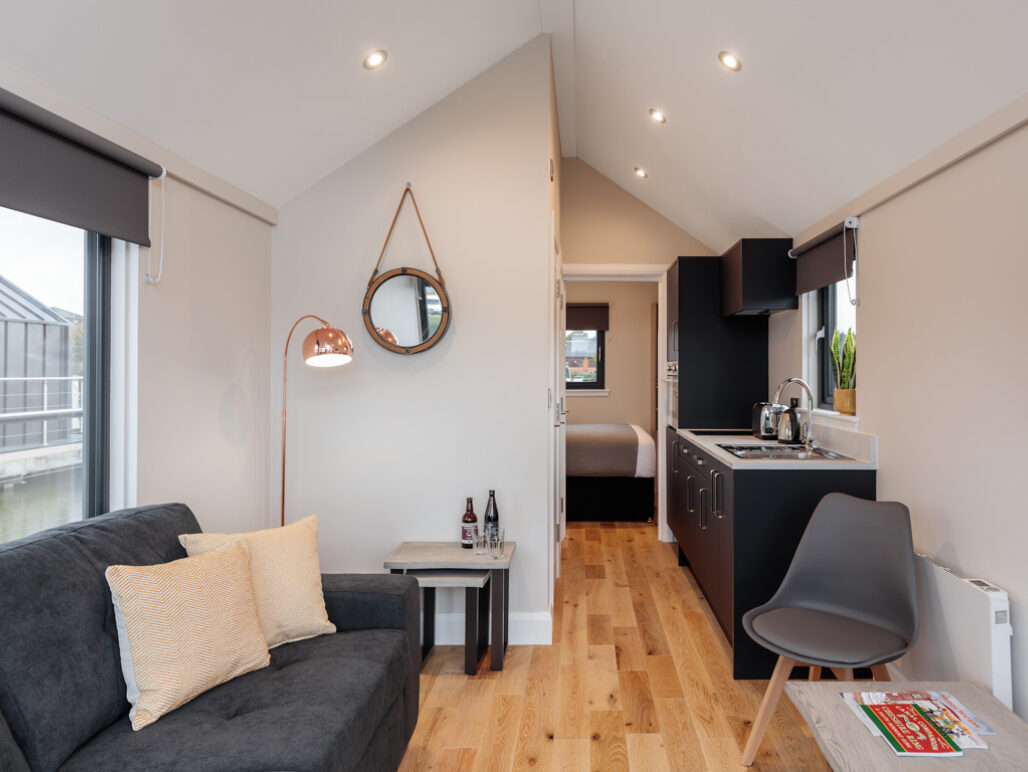 Living / kitchen area with sofa, table, chairs and lamp looking down to back of houseboat towards the bedroom